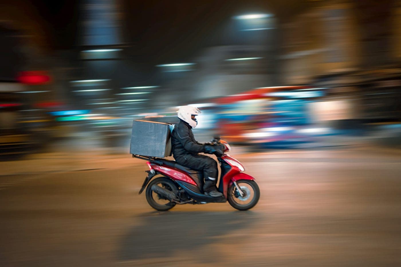 Entregador de moto com baú de entrega à noite