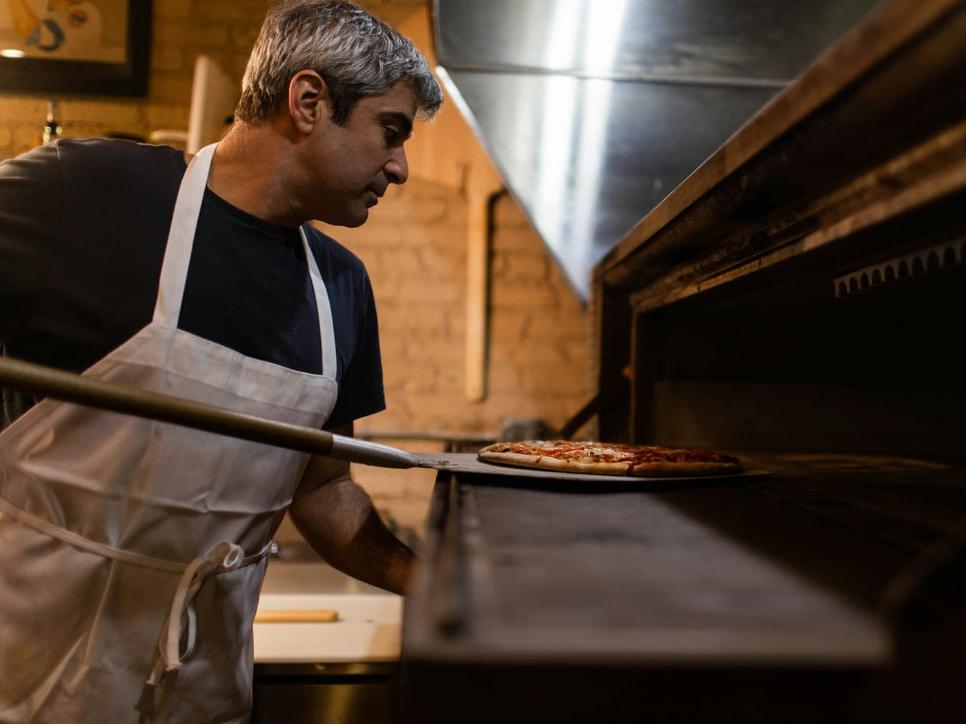 Pizzaiolo colocando uma pizza no forno a lenha